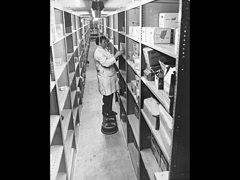 A warehouse worker stands on a kick stool to select stock down a long, neatly organised aisle at Newey & Eyre Ltd's electrical wholesaling premises on Old Heath Road in December 1969. By adding an innovative mezzanine floor, the firm expanded its storage capacity to around 25,000 square feet, creating its third and largest site in Wolverhampton. Connected by a vertical conveyor to transfer stock across levels, the modern facility was designed to optimise space and streamline supply operations for the region's electrical trades. Do you remember visiting or working at the Newey & Eyre warehouse on Old Heath Road during its early days?