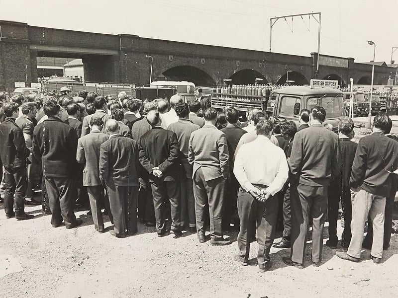 Striking workers gather for a mass meeting outside the British Oxygen Company (BOC) depot on Lower Walsall Street in Wolverhampton in June 1969. With gas cylinder delivery lorries parked idle near the railway arches, employees listen to trade union representatives address the crowd regarding ongoing labour disputes. The tense gathering illustrates the broader industrial unrest and active organised labour movements that frequently swept through major manufacturing and distribution hubs across the West Midlands during the late 1960s. Do you remember the British Oxygen depot or the industrial strikes that affected local businesses around Walsall Street in Wolverhampton in 1969?