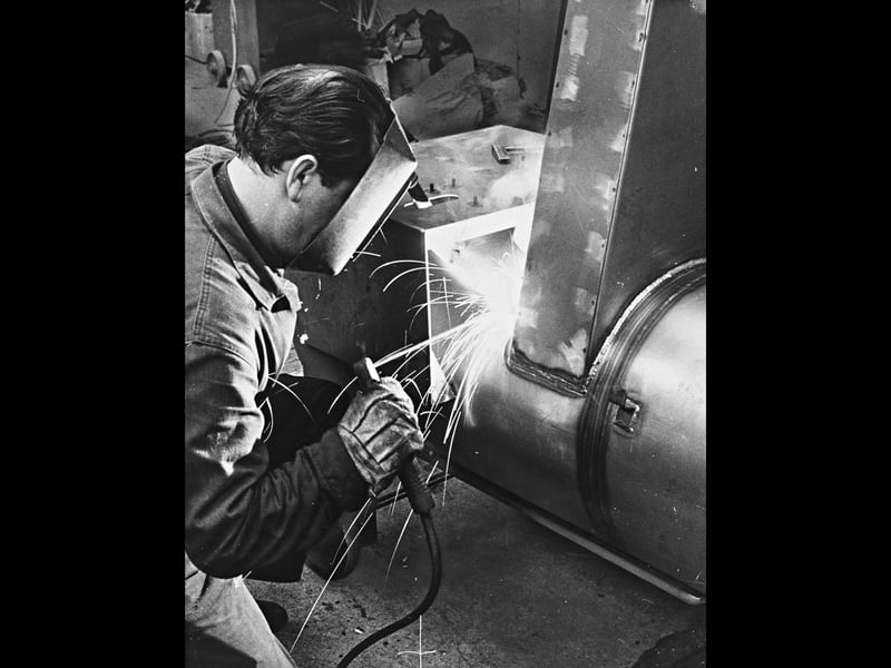 Protective visor in place, a welder focuses intently as sparks shower around a heavy steel housing at Modern Devices Limited in June 1969. The skilled craftsman is pictured finishing the fabrication of a high-pressure washing machine, designed specifically for cleaning commercial vehicles. The striking industrial scene showcases the robust manufacturing and specialised engineering capabilities that defined Wolverhampton's busy post-war factory floors. Did you or someone in your family work in heavy fabrication or welding around Wolverhampton during the late 1960s?
