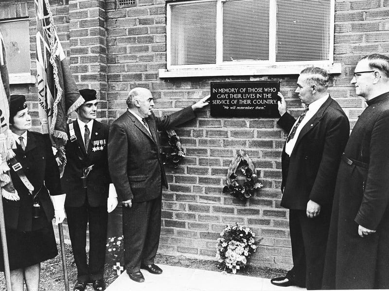 Members and clergy gather for the unveiling and dedication of a new memorial plaque at the Lanesfield branch of the Royal British Legion in September 1969. Presented by the branch's women's section to honour those who gave their lives in service of their country, the dark plaque was mounted on the exterior brick wall alongside memorial wreaths and standard bearers. Present for the unveiling ceremony were branch chairman Mr Geoff Deakin, branch president Mr Harry Dando, and the Rev. John Bigby, who conducted the service of dedication. Do you have family connections to the Lanesfield Royal British Legion branch or remember attending dedication ceremonies like this in Wolverhampton?