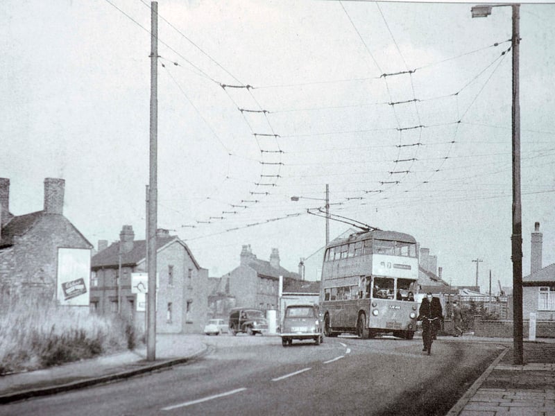 A double-decker trolleybus navigates the busy junction connecting Moxley Road, Pinfold Street, and Dangerfield Lane at Catherine's Cross in Darlaston in 1963. Overhead power lines crisscross above the roadway, guiding the electric transport alongside contemporary motorcars, a cyclist, and traditional brick housing. Capturing a classic slice of Black Country transit history, the scene highlights everyday commuting shortly before trolleybus networks were phased out across the region in favour of diesel buses. Do you remember riding the trolleybuses through Catherine's Cross or travelling around Darlaston back in the early 1960s?