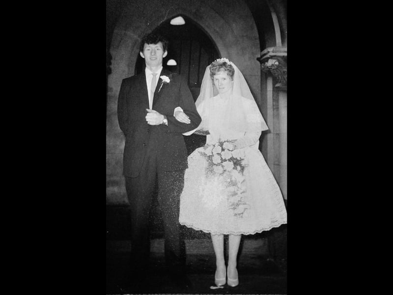 Tom and Beryl Askey emerge beam-to-beam from Christ Church in Blakenall following their wedding service in 1960. The bride looks stunning in a classic tea-length gown, tiered veil, and elaborate bouquet, while the groom looks dashing in a tailored suit adorned with a buttonhole. Standing beneath the stone archway of the parish church, the newlyweds capture a lovely slice of local romance and traditional Black Country wedding charm. Were you married at Christ Church in Blakenall or do you remember attending a wedding reception nearby?