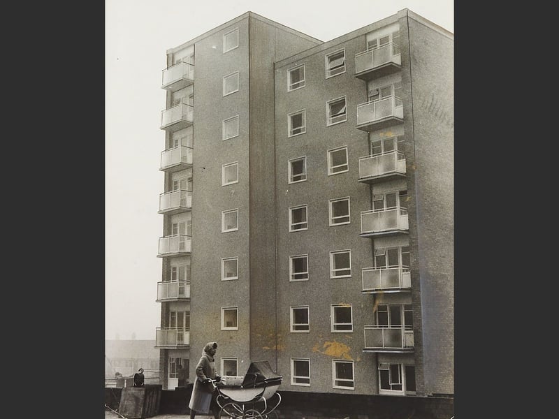 A mother pushes a traditional pram past the brand-new multi-storey block of flats built by Brownhills Urban District Council, officially opened on 16 December 1961. Soaring above the surrounding neighbourhood, the modern high-rise represented a bold step forward in post-war municipal housing, offering local families private balconies, modern amenities, and far-reaching views across the district. Designed to relieve housing pressure, the impressive scheme stood as a proud landmark for the local authority during an era of rapid civic development. Were you living in Brownhills when the council unveiled these new high-rise homes?