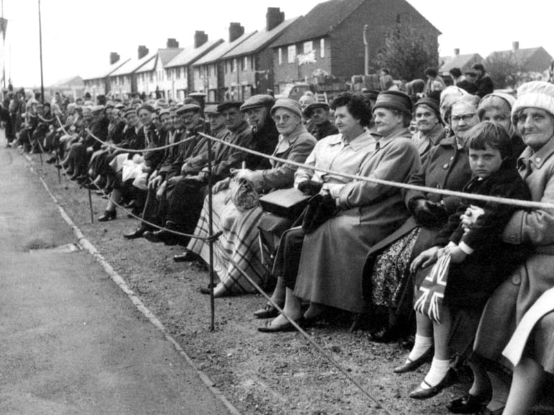 Wrapped in heavy coats and blankets, eager residents line the roadside on makeshift seats, holding Union Jacks as they await the arrival of Her Majesty Queen Elizabeth II during her royal tour of Walsall in May 1962. Neighbours from across the local housing estate gathered along the roped-off pavement hours in advance, determined to secure the best vantage point for a brief glimpse of the monarch. The visit brought a tremendous sense of occasion, celebration, and community pride to families right across the borough. Do you recognise this particular street?