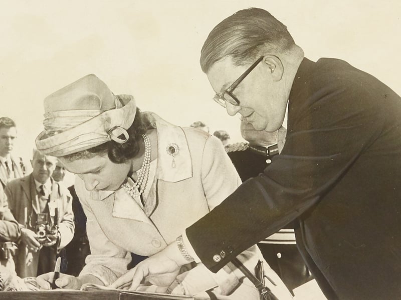 Her Majesty Queen Elizabeth II signs the official Willenhall visitors' book during her royal tour on May 25, 1962. Looking on attentively is Mr J. R. Riding, Clerk of the Willenhall Urban District Council, who guides the book as the monarch completes the ceremonial signing. The historic moment took place during the Queen’s visit to Wednesfield and the surrounding Black Country, drawing eager crowds of local residents and press photographers thrilled to welcome royalty to the area. Do you remember turned out to catch a glimpse of the Queen during her 1962 visit to the district?