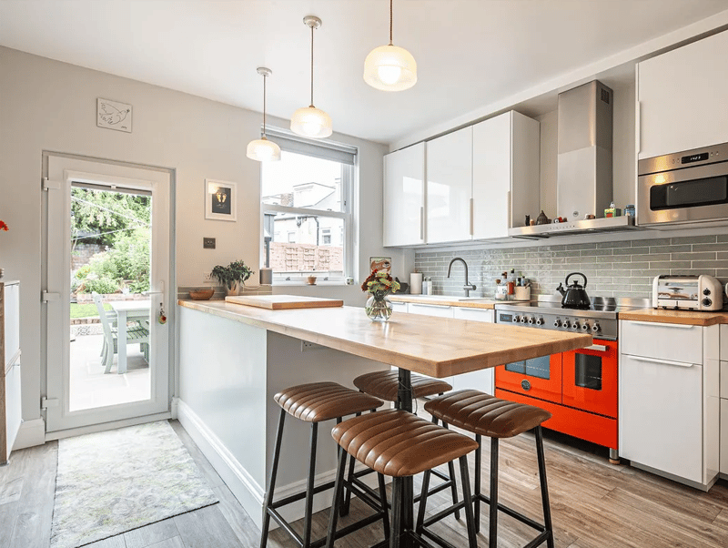 A sleek kitchen features a central island/breakfast bar, range oven and plenty of light from the garden.