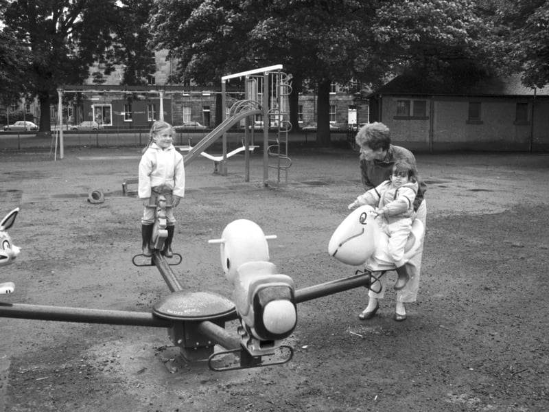 A mother and children playing on the roundabout at the new playground in the East Meadows, Edinburgh, August 1985. 