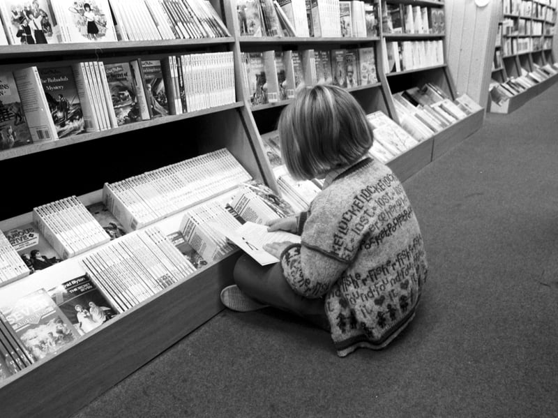 A little girl sitting cross-legged on the floor of James Thin's bookshop reading her book in October 1986.