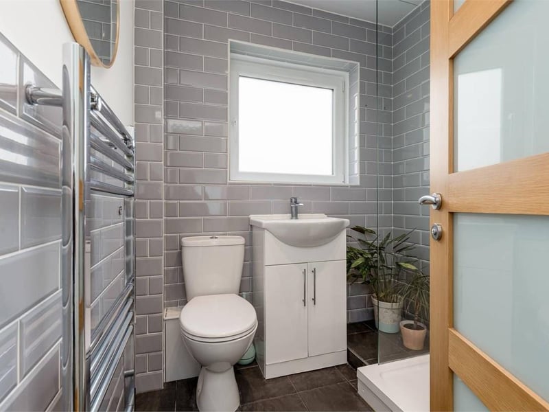 The modern shower room includes a large shower enclosure, WC and washbasin with vanity storage, complemented by predominantly tiled walls and flooring.