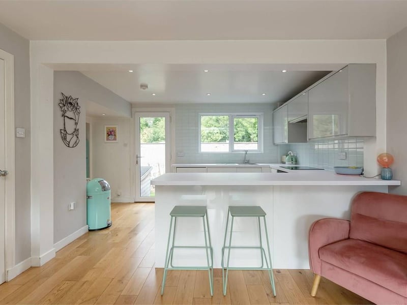 The contemporary kitchen is fitted with white gloss units, laminate worktops and tiled splashbacks, together with an electric ceramic hob, fan-assisted oven, dishwasher and fridge freezer.