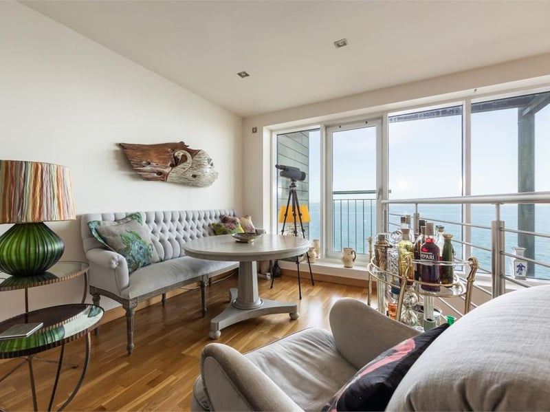 An open timber staircase connects the dining room with the lounge above, giving the apartment a distinctive two-level arrangement. The lounge has waterfront glazing and a Juliet balcony.