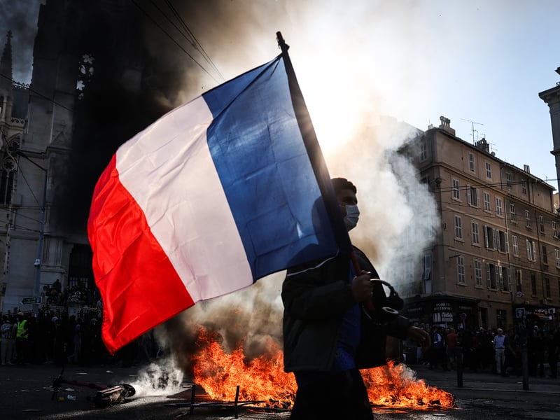 A protester waving a French national flag walks past a fire during clashes prior to the start of a demonstration to protest against the "high cost of living", in Marseille