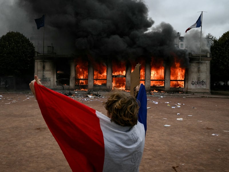 A protester wrapped in a French national flag stands in front of Lyon's tourism office set on fire during a demonstration 