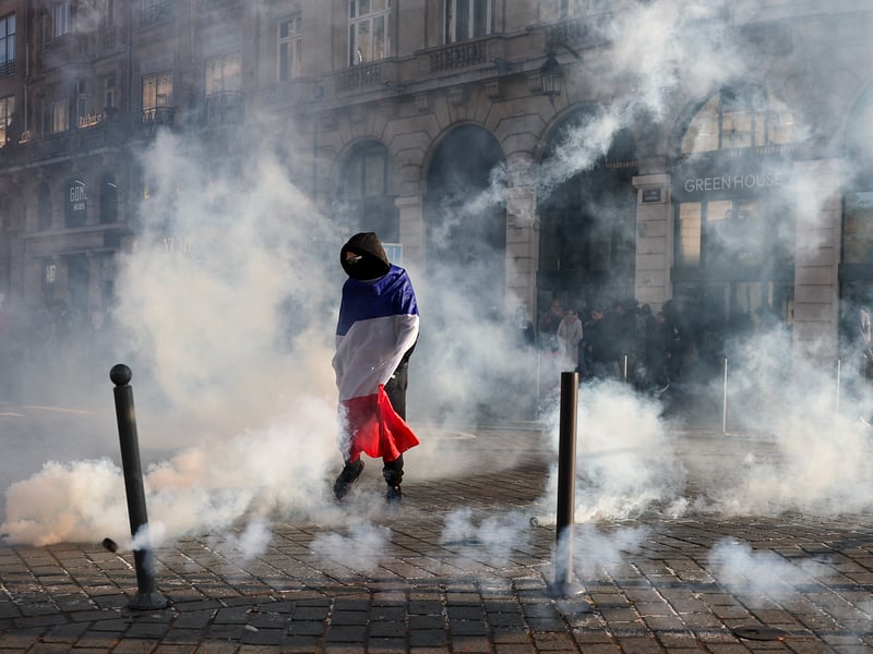 A protester, wrapped in a flag of France, stands in the smoke at Place de l'Opera during ongoing protest action against the "high cost of living", in Lille.