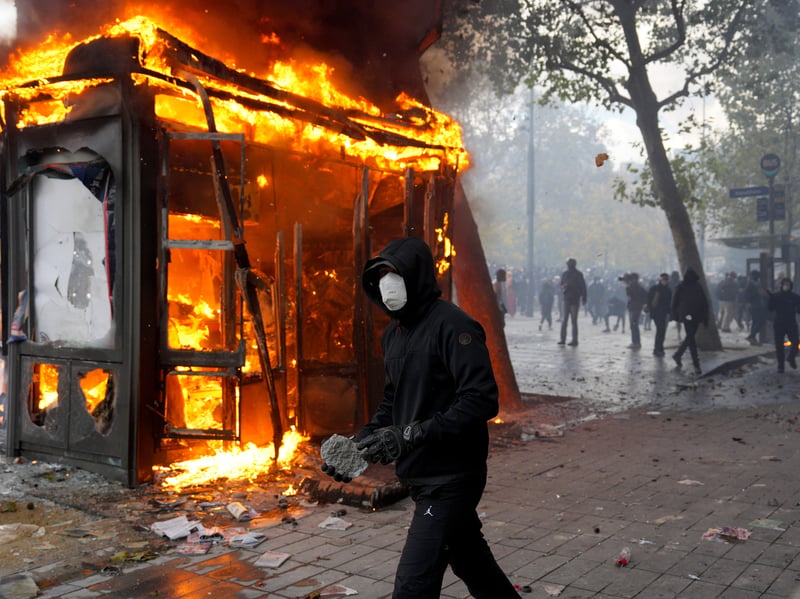 A protester holds a rock as a kiosk burns during a demonstration near Place de la Republique