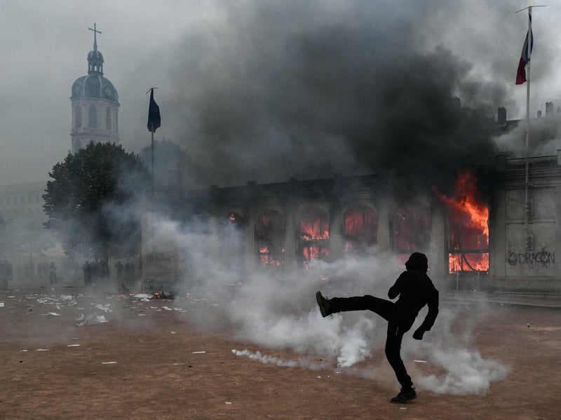 A protester kicks a projectile as he stands among tear gas in front of Lyon's tourism office.
