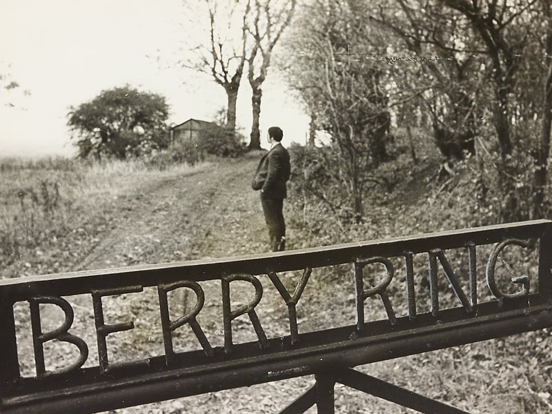 Standing beyond a wrought-iron gate marked with the words BERRY RING, a solitary visitor gazes toward the ancient hill fortress on the outskirts of Stafford on October 31, 1970. The site sparked local debate over whether it should be called Bury Ring or Berry Ring, as roadside signs and Ordnance Survey maps offered conflicting spellings. Local historian Sidney Horne of Rowley Park clarified the mystery, explaining that Bury is historically correct based on the ancient fortress constructed around 700 BC. Do you remember visiting Berry Ring or exploring ancient earthworks and hillforts around Staffordshire? Did you ever notice the conflicting road signs and place names around the outskirts of Stafford back then?
