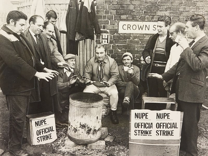 Striking refuse collectors gather around a burning dustbin to keep warm outside the Crown Street depot of the Wolverhampton Cleansing Department on October 9, 1970. Placed alongside official National Union of Public Employees (NUPE) placards, the improvised brazier provided much needed relief for workers standing picket duty during autumn industrial action. The atmospheric shot captures the solidarity and makeshift spirit of public service workers taking a stand during a turbulent era for British labour relations. Do you remember the NUPE public service strikes or seeing picket lines set up outside local council depots in autumn 1970? How did the disruptions affect everyday services around Wolverhampton at the time?