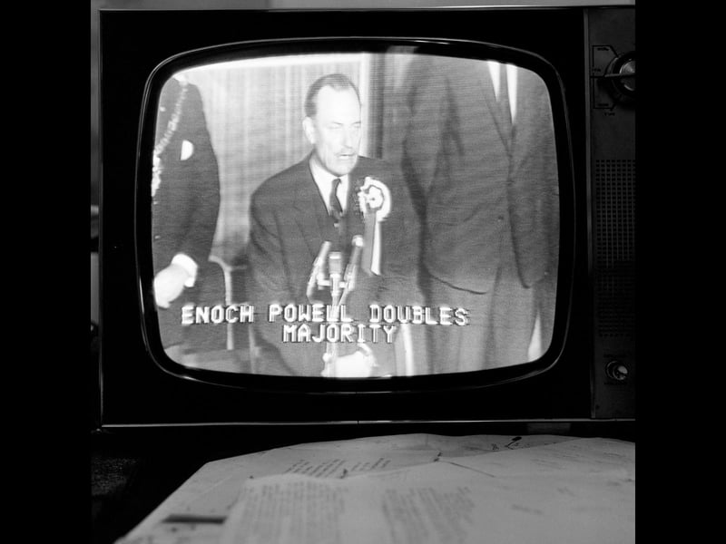 Flickering on a classic black-and-white television set, Conservative MP Enoch Powell addresses local voters after being returned to Parliament for the Wolverhampton South West constituency on June 18, 1970. Wearing a large rosette and speaking into a bank of microphones, Powell made national headlines as the TV screen graphic declared that he had doubled his majority. Captured mid-broadcast beside dial controls and news scripts, the image evokes the dramatic election nights of the era when families across the region gathered around the television set to watch the political drama unfold late into the night. Do you remember staying up late to watch the general election returns on television back in June 1970? What are your memories of following local political news around town during that time?