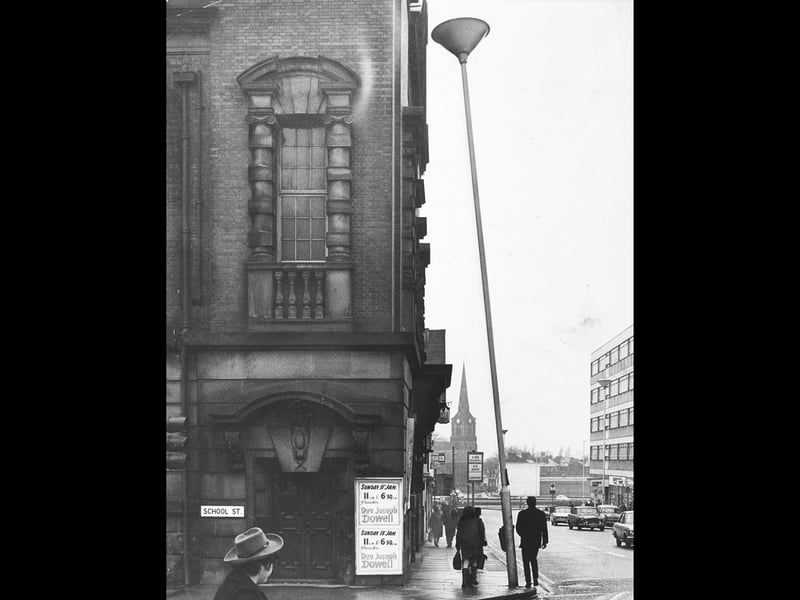 A distinctly wonky street light tilts at a precarious angle beside the Darlington Street Methodist Church at the corner of School Street in Wolverhampton on January 12, 1970. The unusual slant prompted an amused letter to the editor of the Express & Star from a local resident, who joked that George Formby himself must have leaned on the post to push it so far out of line. Pedestrians in hats and winter coats pass beneath the grand stonework and noticeboards advertising upcoming sermons by Rev Joseph Dowell, with the spire of St Peter's Church rising gracefully in the background. Do you remember walking past the famously leaning lamp-post on Darlington Street back in 1970? What other quirky street details or memorable sights around the town centre do you recall from those days?