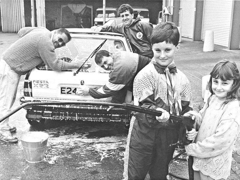 Powering through a sudsy charity challenge! On September 26, 1992, hard-working car washers Kevin Hunt, Graham Kemsley, and Mick Kemsley clean down a Ford Fiesta XR2 alongside young helpers Brian Cullen and Truudi Kemsley during a community car wash at the council's Lammascote Road depot in Stafford. Organized by the borough council cleansing department staff alongside local cubs and scouts, the energetic team armed themselves with sponges, buckets, and pressure washers to raise essential funds for the county's air ambulance service.