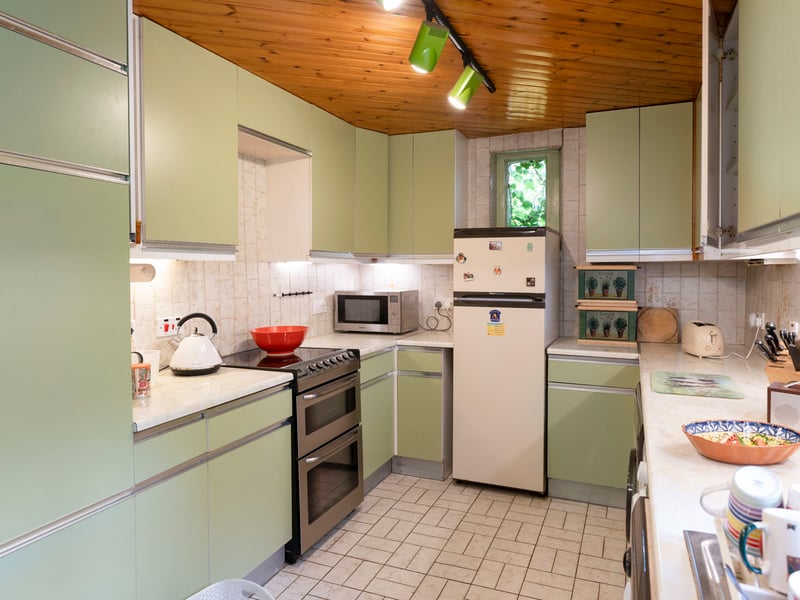 The kitchen offers excellent scope for contemporary redesign, while remaining fully functional with fitted cabinetry, downlit worktops, and freestanding appliances comprising an electric cooker, washing machine, tumble dryer, and tall fridge freezer. 