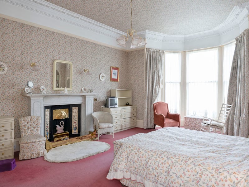 The generous first-floor principal bedroom beautifully combines character and comfort, with a wide bay window, ornate cornicing, and a period fireplace. 