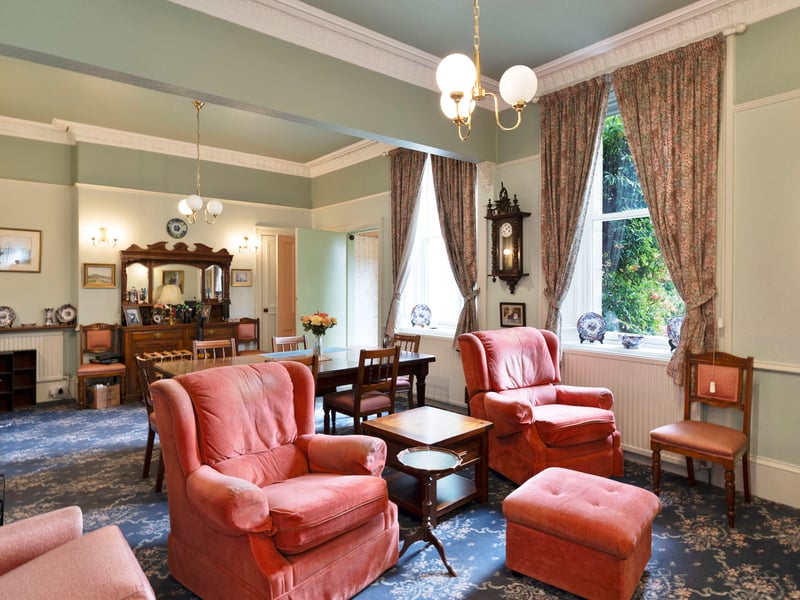 To the rear, the open-plan dining and sitting room spans the width of the home, with a garden outlook and direct kitchen connection. Further period detailing includes ornate cornicing and a colourful tiled fireplace with a living-flame fire, while both spaces provide built-in storage.