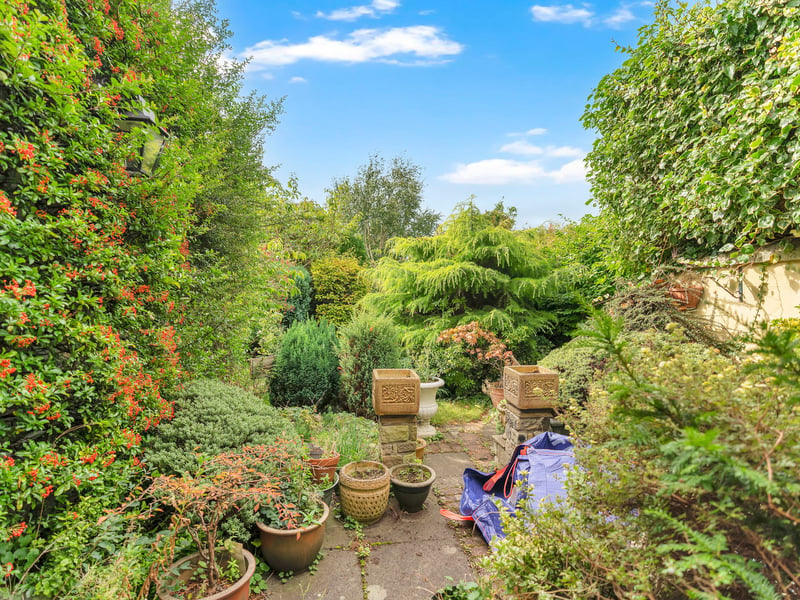 Established gardens to the front and rear enhance privacy, with mature trees, shrubs, and hedging creating a leafy setting. The enclosed rear garden offers a secluded retreat with lawn, paved areas, and densely planted borders, while the front garden provides an attractive screen from the road.
