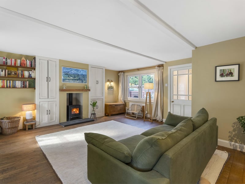 The spacious sitting room enjoys dual-aspect windows, creating a bright and inviting atmosphere, with a wood-burning stove providing a cosy focal point. Useful built-in cupboard storage adds to the practicality of this appealing living space.