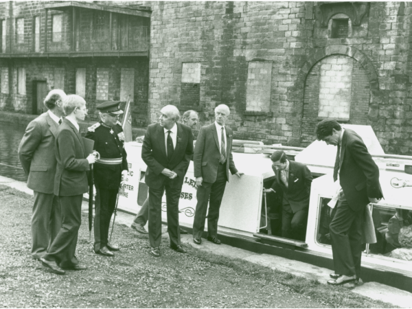 	
Princes Charles exits a canal boat onto the tow path whilst flanked by dignitaries, opposite are the cottages in the Weaver's Triangle.
