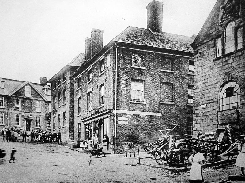 The Castle Hotel, Bishop's Castle, on the left, and The Powis Institute, far right. The sign on the front of the institute is for Greenhous and the junk appears to be agricultural implements. The building was demolished long ago. Note the cross underneath the pram or cart in the centre to mark it out for some reason.