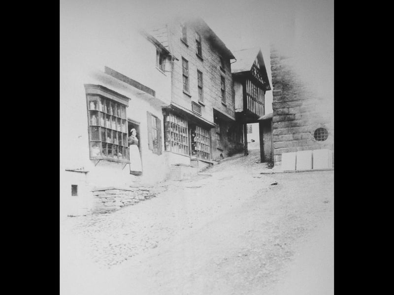 The top of Bishop's Castle High Street, showing the House on Crutches, and a glimpse of the town hall on the right. The woman is standing in the doorway of what used to be Ross's shoe shop, but it looks like it was a sweet shop in her day.
