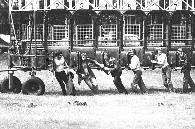 Straining muscles, grassy turf, and numbered metal gates, this July 1982 photograph captures stall handlers using sheer shoulder power to move the heavy starting stalls into place at Dunstall Park racecourse. With a race meeting about to get under way, the crew jumped inside the traps to manually guide the massive wheeled structure across the course. Some worked in open collared jackets while others went bare chested in the summer heat, offering an energetic, behind the scenes glimpse of the hard physical graft keeping Wolverhampton horse racing running smoothly. Do you remember spending a summer afternoon watching the horses run at Dunstall Park back in 1982? Who recalls seeing the grounds crew out on the course manhandling those heavy starting stalls into position?