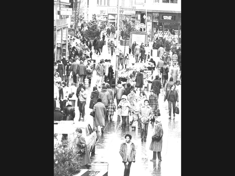 Rain slicked paving, heavy winter coats, and a sea of eager shoppers fill the pedestrianised stretch of Dudley Street on the final Saturday before Christmas in December 1982. Despite economic worries across the nation, high street tills rang constantly as local residents crowded into town to snap up festive luxury gifts. Department stores and electrical outlets like Woolworths found themselves overwhelmed by record demand, with audio visual counters swiftly selling out of portable colour televisions, hi fi audio systems, and cassette tape recorders to festive shoppers eager for the latest gadgets. Do you remember braving the packed crowds on Dudley Street for that last minute Christmas shopping dash back in 1982? Did you pick up an early video player, television, or cassette deck as a festive treat that winter?