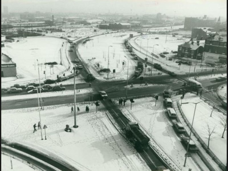 A blanket of snow and treacherous ice covers Wolverhampton in January 1982, captured here in a bird's-eye view looking down over a major junction of the ring road. Motorists crawl through narrowed, slushy lanes while pedestrians carefully trace frozen footpaths across the carriageway during one of the coldest snaps of the decade. Do you remember navigating the treacherous roads and sub-zero freeze across the town during the big snow of January 1982?