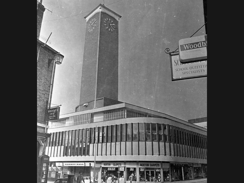The distinctive '60s architecture of the Shrewsbury Market Hall and its soaring Mardol clock tower dominate the street corner in 1979, framed by familiar shopfront signs for local businesses like Brooks Shoe Salon and Norton Carpets in a photograph captured by Walter Winder. Do you remember when the clock tower and modern market building were a relatively fresh addition to the Shrewsbury skyline? Which shops along Bellstone, Shoplatch, or inside the Market Hall itself did you visit most often during those years?