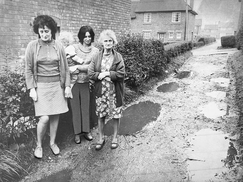 Standing beside waterlogged ruts and deep puddles, Upper Gornal residents gaze in frustration at the unpaved track running between their homes in November 1974. Pictured outside are Joan Monkton, her daughter Mrs K Harrison holding young Michael Harrison (of 25 Tudor Road), and neighbour Mrs C Fidler from No. 23, all protesting the dreadful condition of the footpath connecting Tudor Road with Tudor Vale. Churned into a muddy morass by passing tradesmen’s vans and heavy lorries, the neglected alleyway left householders fed up with ruined footwear, splashing traffic, and a total loss of privacy—prompting Dudley West MP Dr Colin Phipps to take their plight straight to Dudley Council. Do you remember navigating the muddy pathways around Tudor Road, or recall the community campaign to get Upper Gornal's tracks surfaced back in the 1970s?